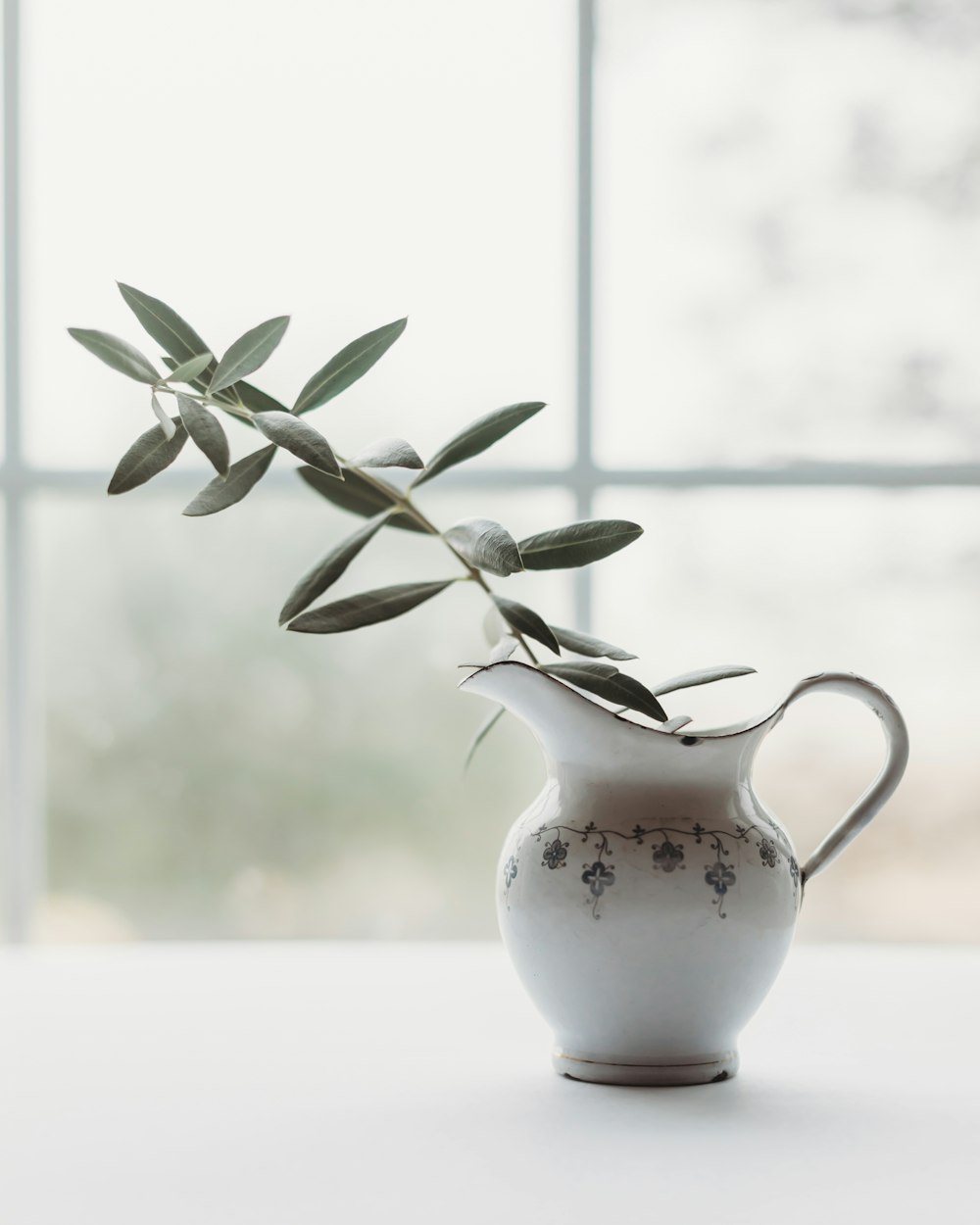 a white vase with an olive branch in it