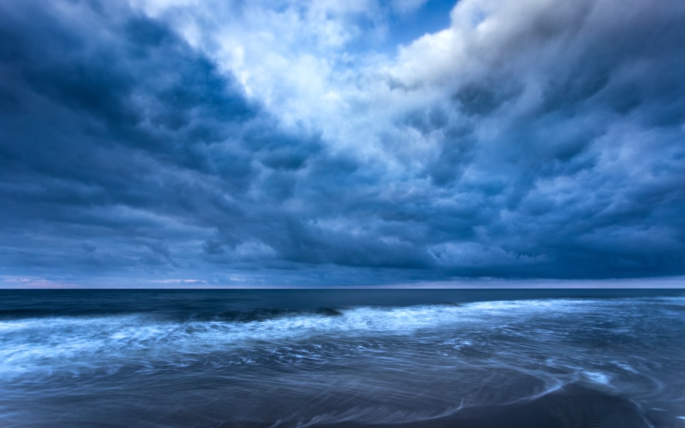 a cloudy sky over the ocean with waves coming in