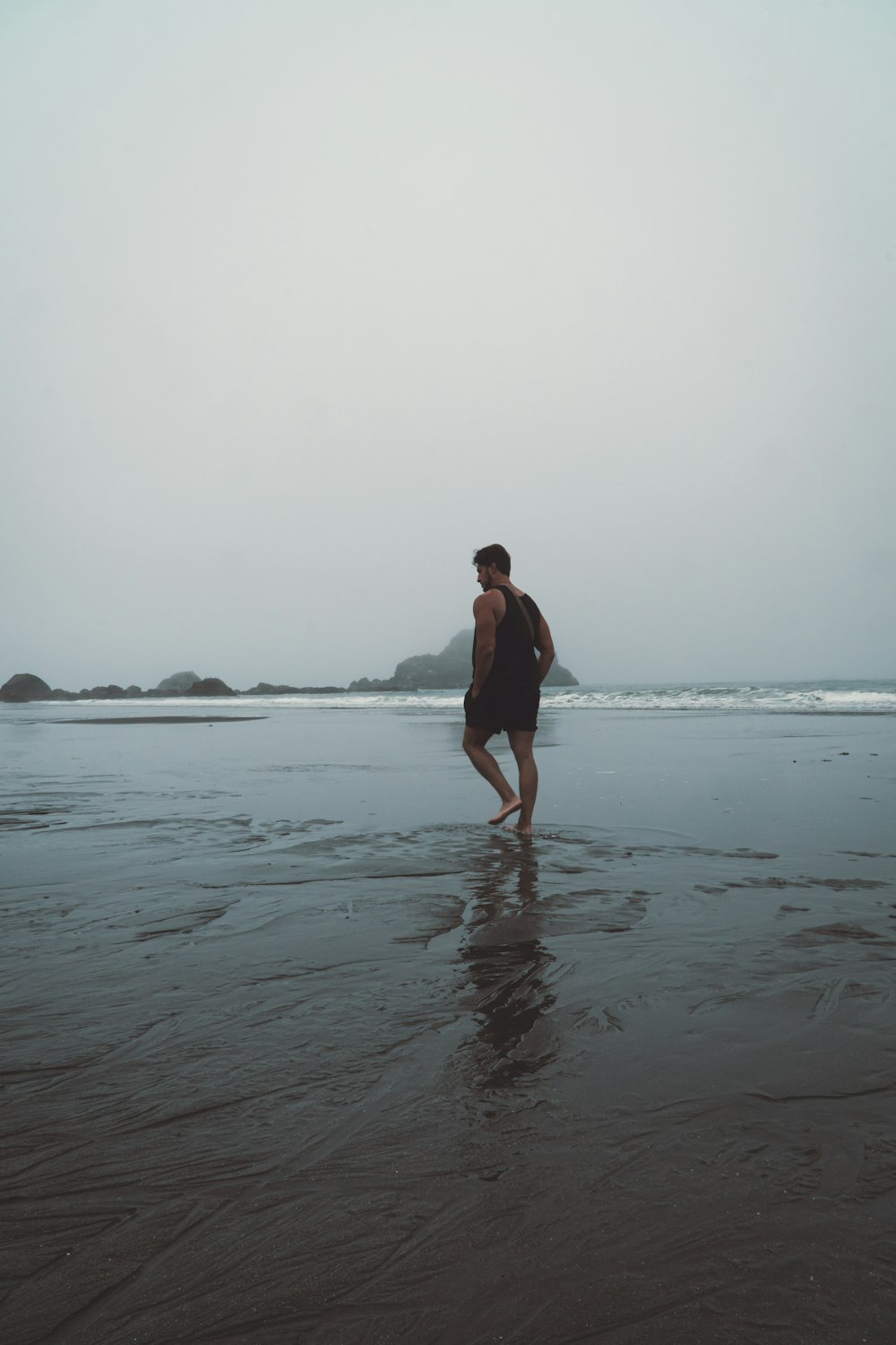a man standing on top of a wet beach next to the ocean