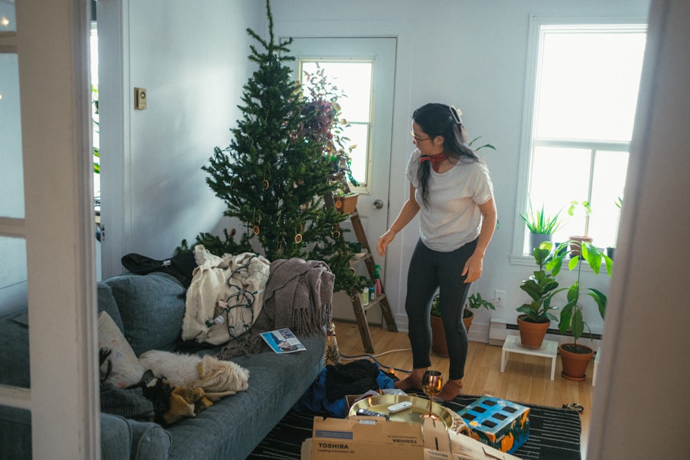 a woman standing in a living room next to a christmas tree