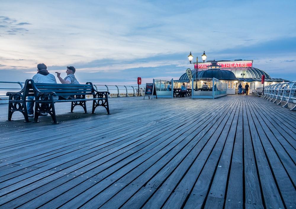 two people sitting on a bench on a pier