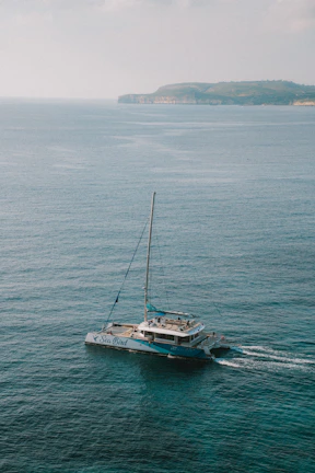 Bob piloting a helicopter over turquoise waters with the catamaran visible below.