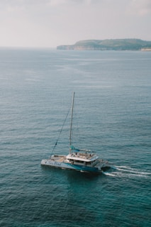 A catamaran with 'Sea Bird' written on its side sails through calm, turquoise waters with an island visible in the distant background under a lightly clouded sky.