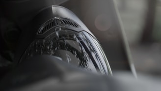 Close-up of a reflective motorcycle helmet visor with a soft focus background. The visor shows reflections of the surrounding greenery, while the top of the helmet includes a vented area.