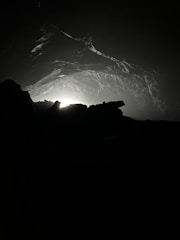 A dimly lit cave interior with rocky formations and a faint light source emanating from the background. Shadows and textures create an ominous and mysterious atmosphere.