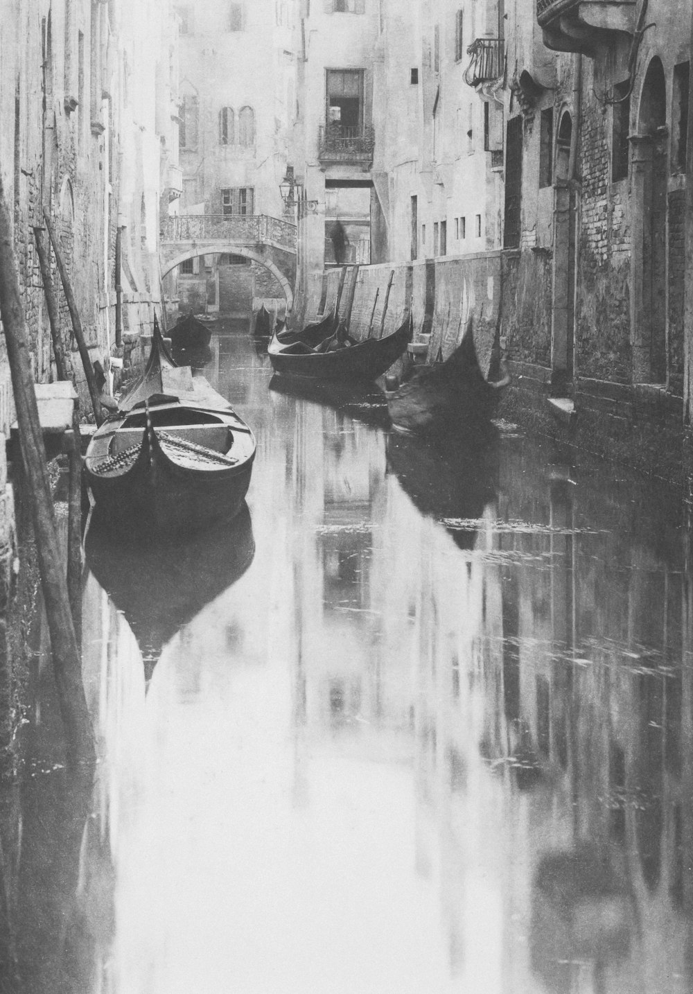 a black and white photo of a canal with boats