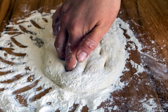A baker’s hands kneading dough on a wooden table dusted with flour.