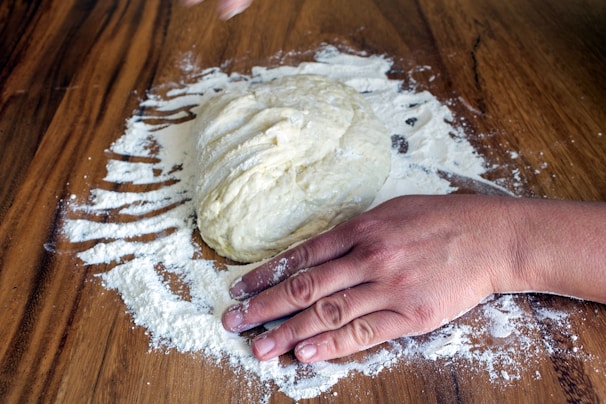 Artisanal corn dough being prepared by hand on a wooden surface with fresh ingredients nearby.