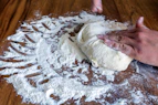 A chef’s hands stretching dough over a wooden board, dusted with flour.