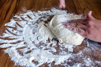 Hands kneading dough made from ancient grains on a floured wooden surface.