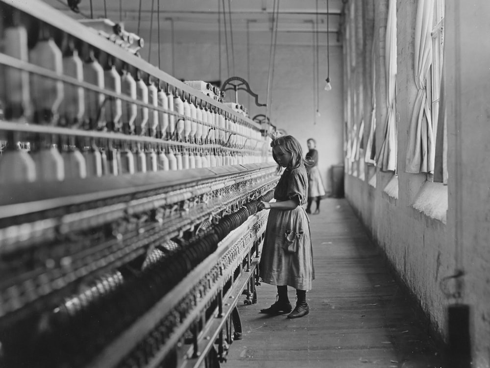 a black and white photo of a woman standing in front of a loom of