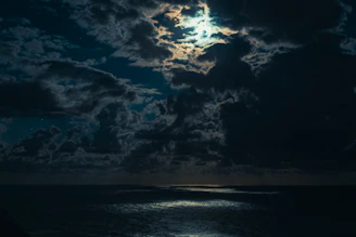 A dark, misty ocean cove illuminated by a faint, eerie glow under a cloudy night sky.