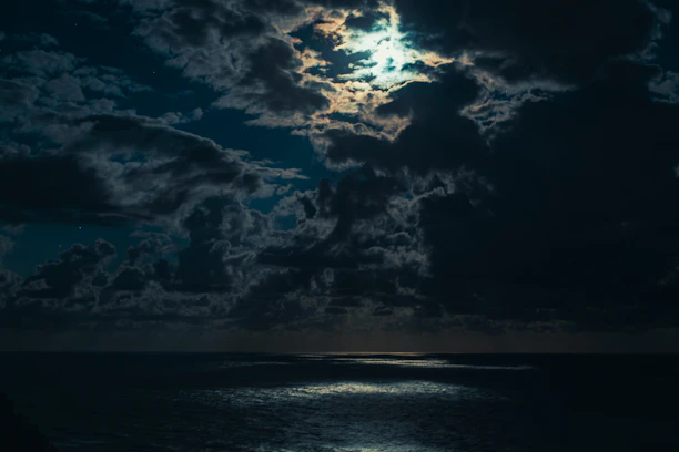 A dark, misty ocean cove illuminated by a faint, eerie glow under a cloudy night sky.