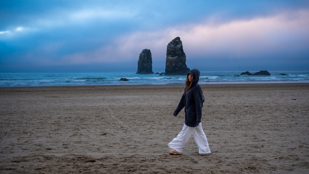 a woman walking across a sandy beach next to the ocean