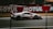 A sleek race car is speeding down a racetrack, with a blurred background that suggests motion. The car is predominantly white with red and black accents and features the number 54 prominently on its side. Advertising and branding are visible, with large logos and designs.