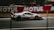 A sleek race car is speeding down a racetrack, with a blurred background that suggests motion. The car is predominantly white with red and black accents and features the number 54 prominently on its side. Advertising and branding are visible, with large logos and designs.