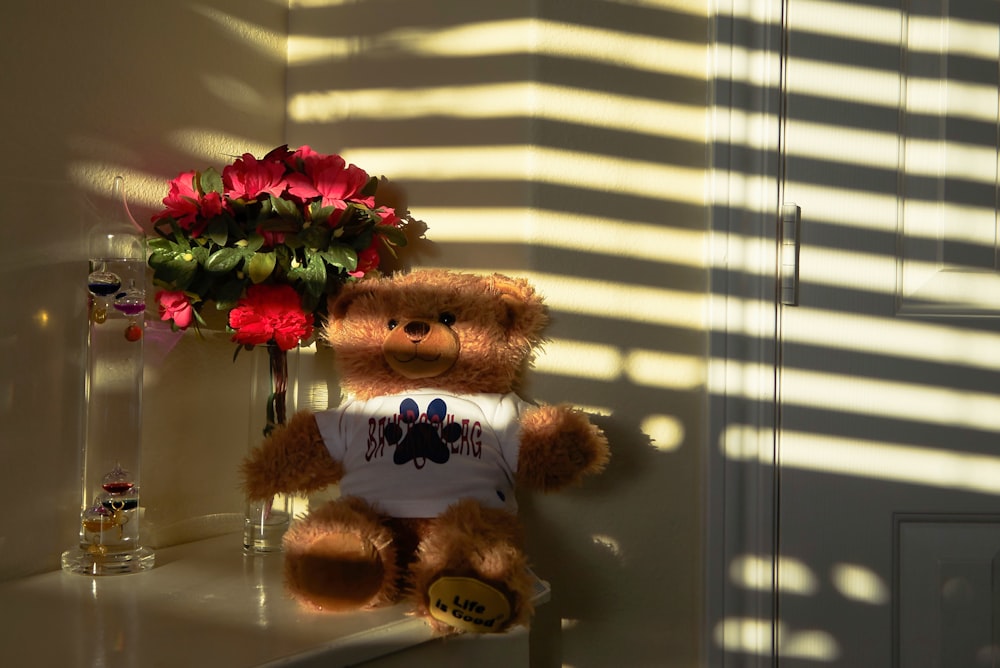 a teddy bear sitting on a shelf next to a vase of flowers
