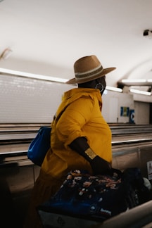 a man in a yellow jacket and hat sitting on a luggage carousel