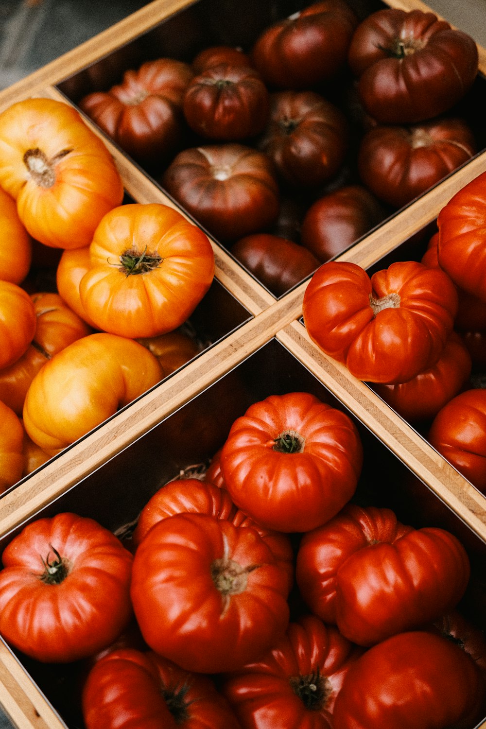 four wooden boxes filled with different types of tomatoes