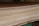 A close-up view of a stack of smooth, evenly cut plywood sheets. The wood grain and layers are visible, indicating high-quality, processed lumber. The sheets are neatly aligned and resting on a green support structure.