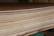 A close-up view of a stack of smooth, evenly cut plywood sheets. The wood grain and layers are visible, indicating high-quality, processed lumber. The sheets are neatly aligned and resting on a green support structure.