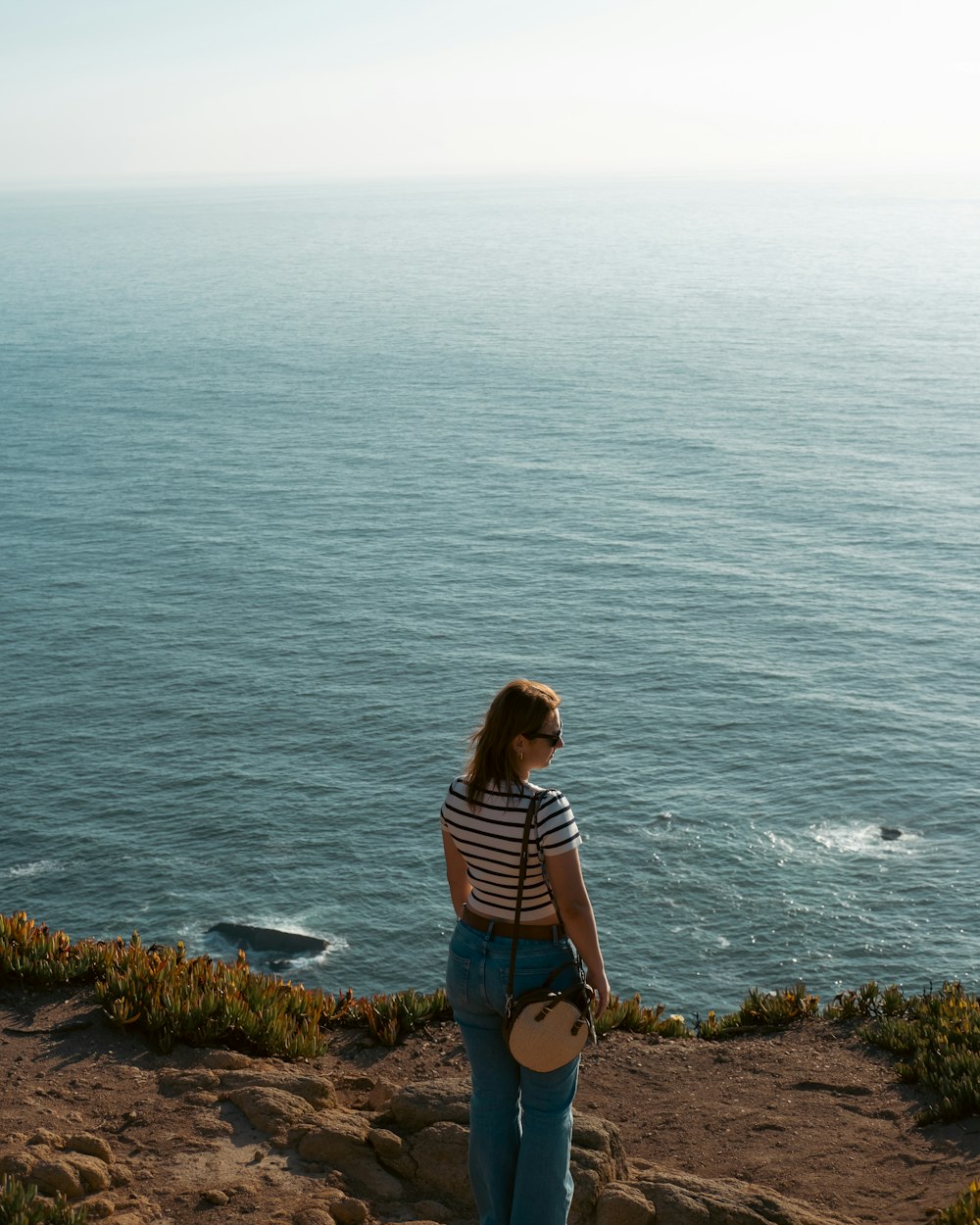 a woman standing on top of a cliff next to the ocean