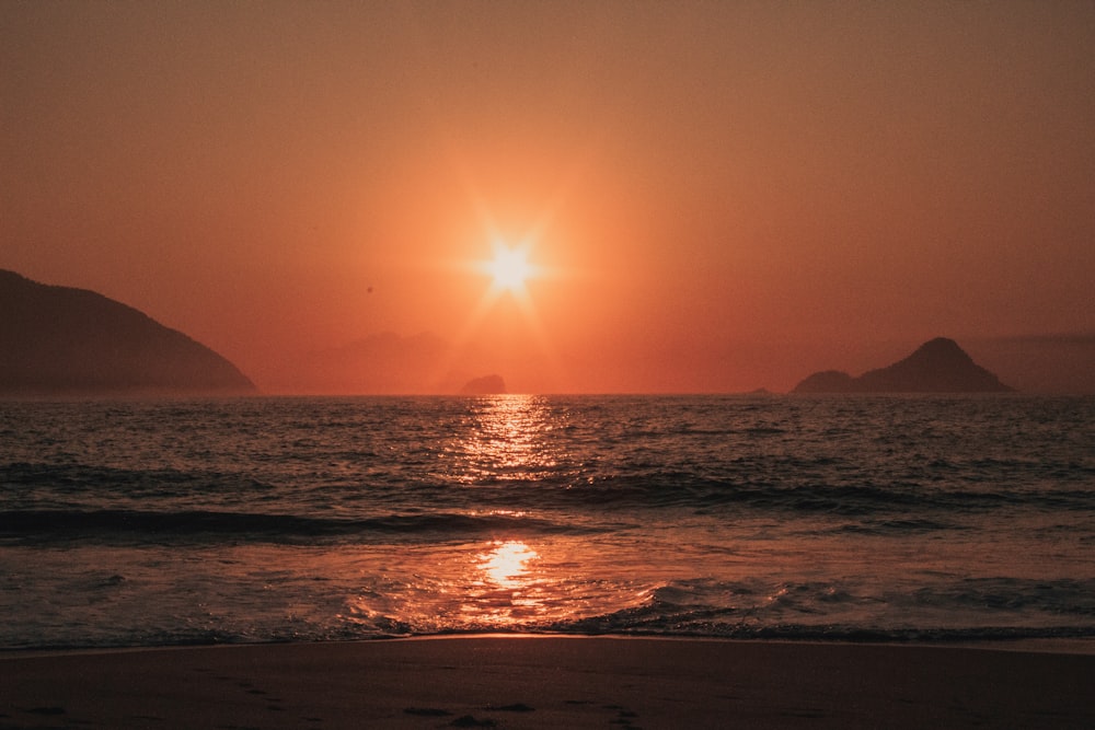 the sun is setting over the water at the beach