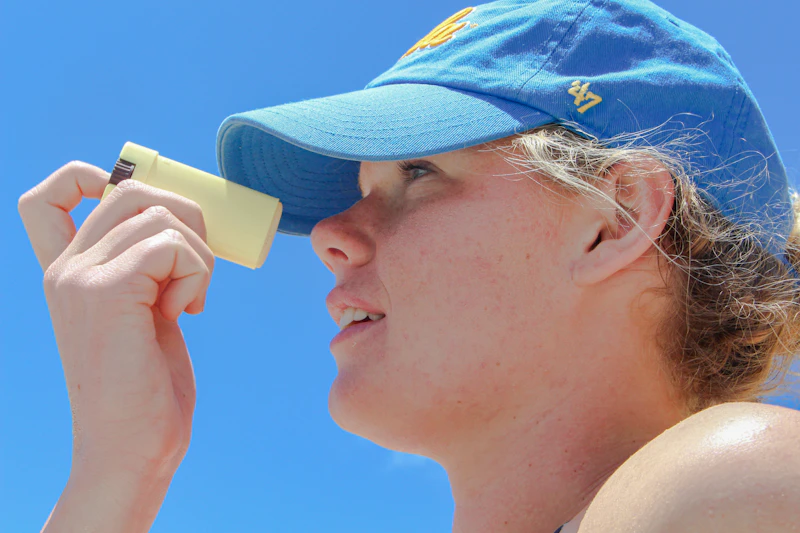 Teen in a blue cap applying a sunscreen stick to their nose