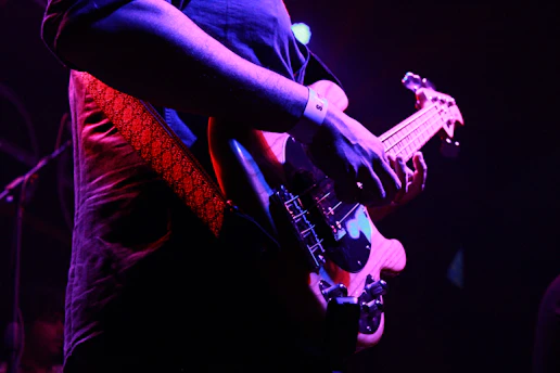 A gritty close-up of a guitarist's hand shredding on an electric guitar under red stage lights.