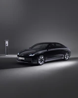 A sleek electric car charging at a modern station in Dhaka during sunset.