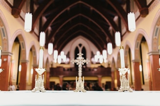 An ornate cross and candlesticks are displayed on an altar inside a church with high vaulted ceilings and Gothic arches. The warm lighting and intricate details of the architecture evoke a sense of reverence and tradition.