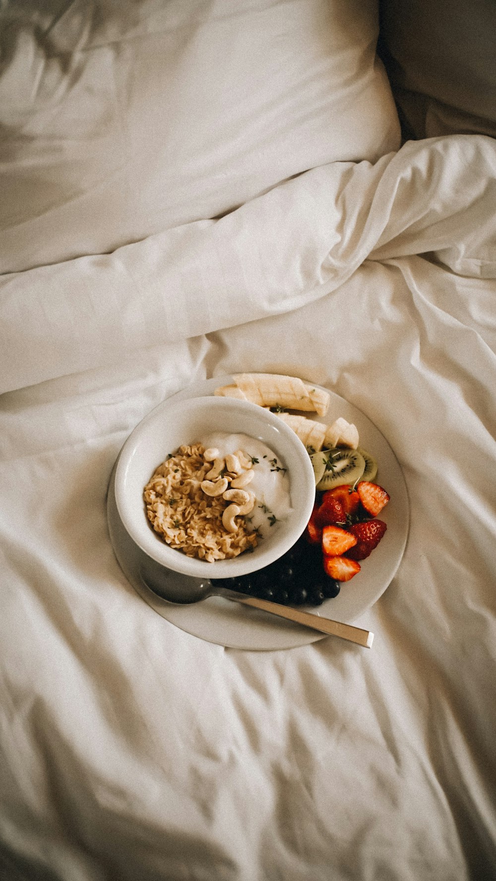 a bowl of oatmeal and a plate of fruit on a bed