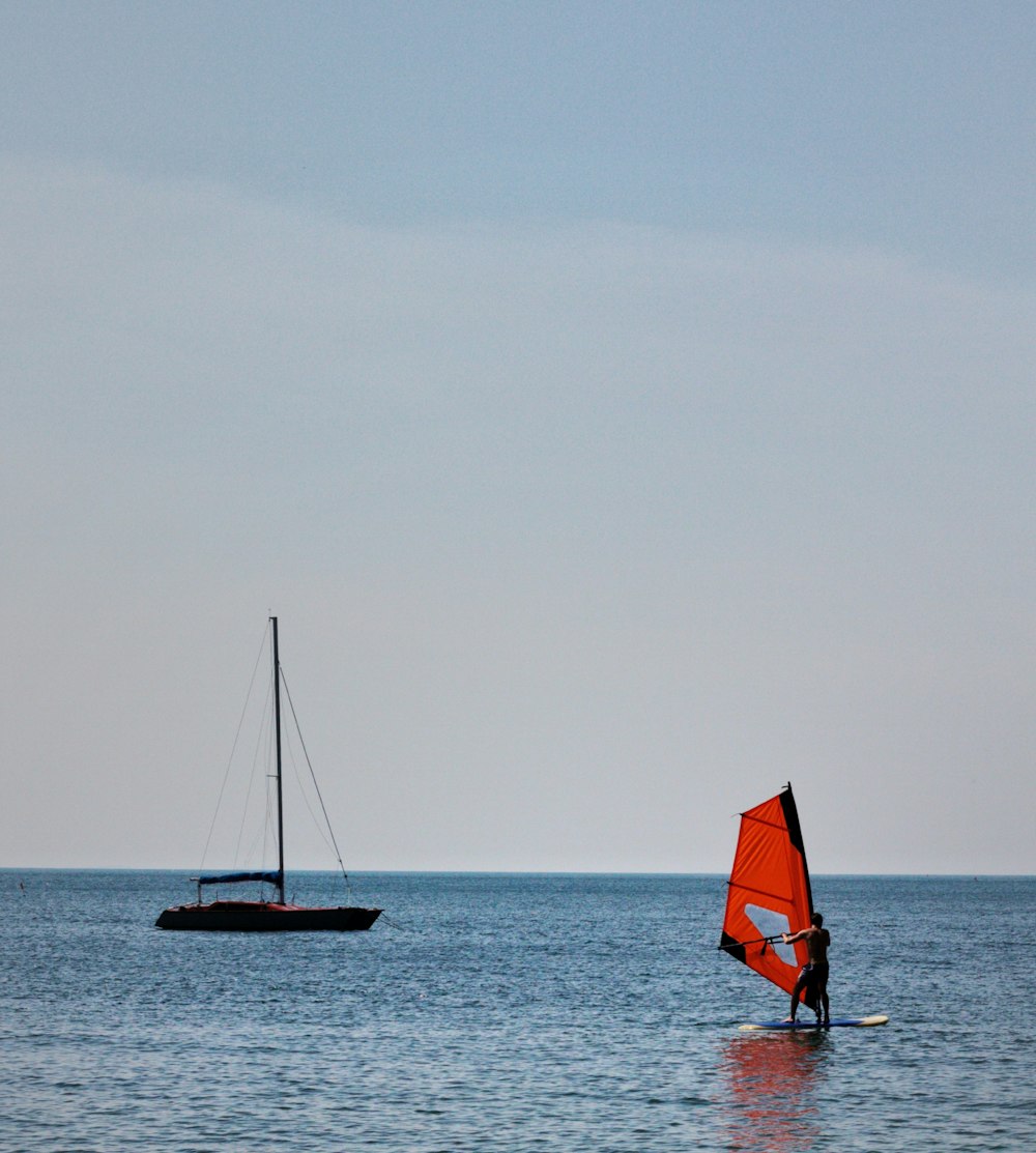 a person on a surfboard with a sail boat in the background