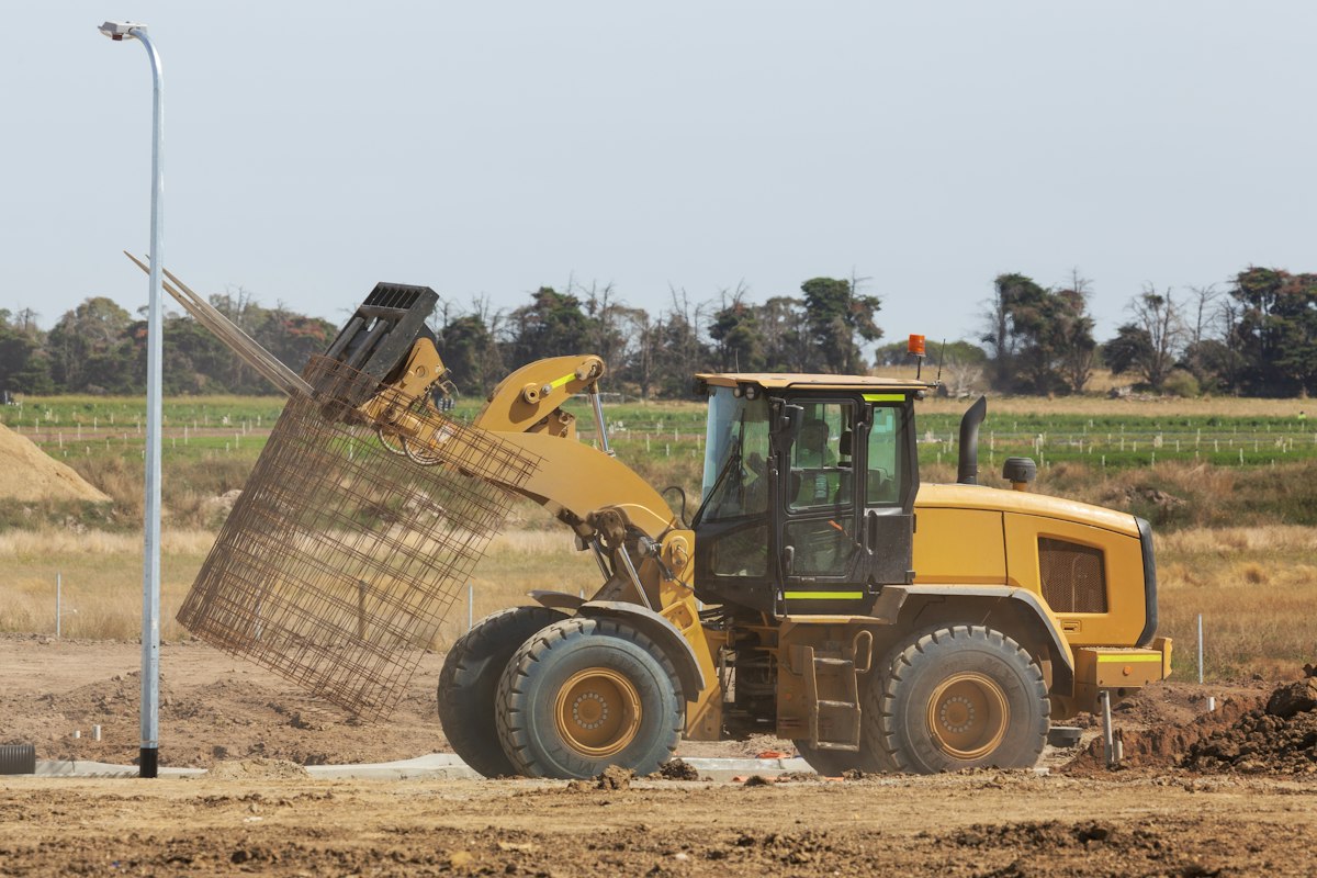 Wheel loader with a raised front bucket on an exposed soil work area.