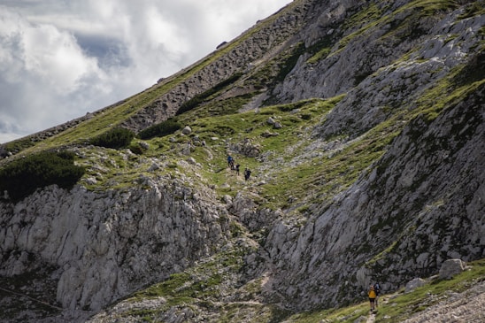 Trail runners ascending a rugged mountain path in the Tarentaise massif with vivid green and orange accents.