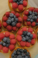 Delicate fruit tarts topped with vibrant berries and a sprinkle of powdered sugar on a dark blue ceramic dish