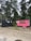 Two small trailers are situated on a sandy area surrounded by tall, green trees. One trailer is painted black with a window and some decorations, while the other is bright pink and appears to be a food stall, with an ice cream cone sign and a menu board.