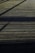 A wooden deck surface with straight horizontal lines accentuated by the planks. Shadows of an unseen structure create diagonal patterns across the deck, giving it a textured appearance.