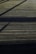 A wooden deck surface with straight horizontal lines accentuated by the planks. Shadows of an unseen structure create diagonal patterns across the deck, giving it a textured appearance.