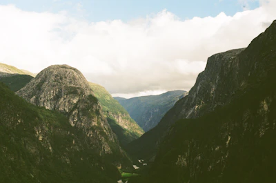 Wide shot of a serene mountain landscape with deep green valleys and a cloudy sky.
