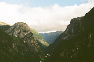 Wide shot of a serene mountain landscape with deep green valleys and a cloudy sky.