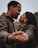 A couple is intimately holding hands, focusing on the woman’s hand adorned with an engagement ring. The two individuals are looking into each other’s eyes, suggesting a moment of connection and affection.