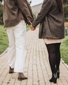 A man and woman walking side by side on a cobblestone street, both dressed in stylish fall layers.