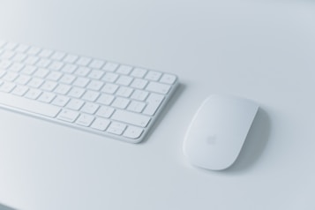 A sleek and modern wireless keyboard placed on a light-colored surface alongside a matching wireless mouse. The minimalist design is complemented by soft lighting, creating a clean and organized workspace feel.