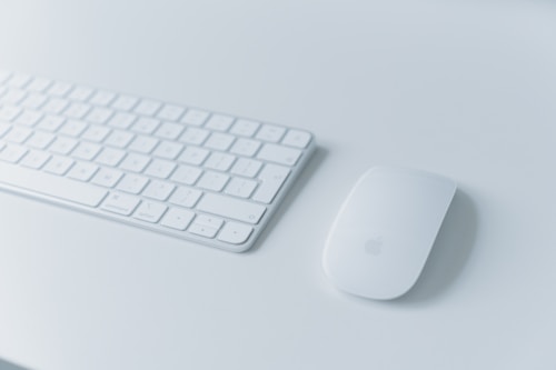 A sleek and modern wireless keyboard placed on a light-colored surface alongside a matching wireless mouse. The minimalist design is complemented by soft lighting, creating a clean and organized workspace feel.