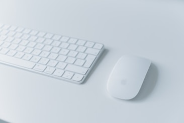 A sleek and modern wireless keyboard placed on a light-colored surface alongside a matching wireless mouse. The minimalist design is complemented by soft lighting, creating a clean and organized workspace feel.