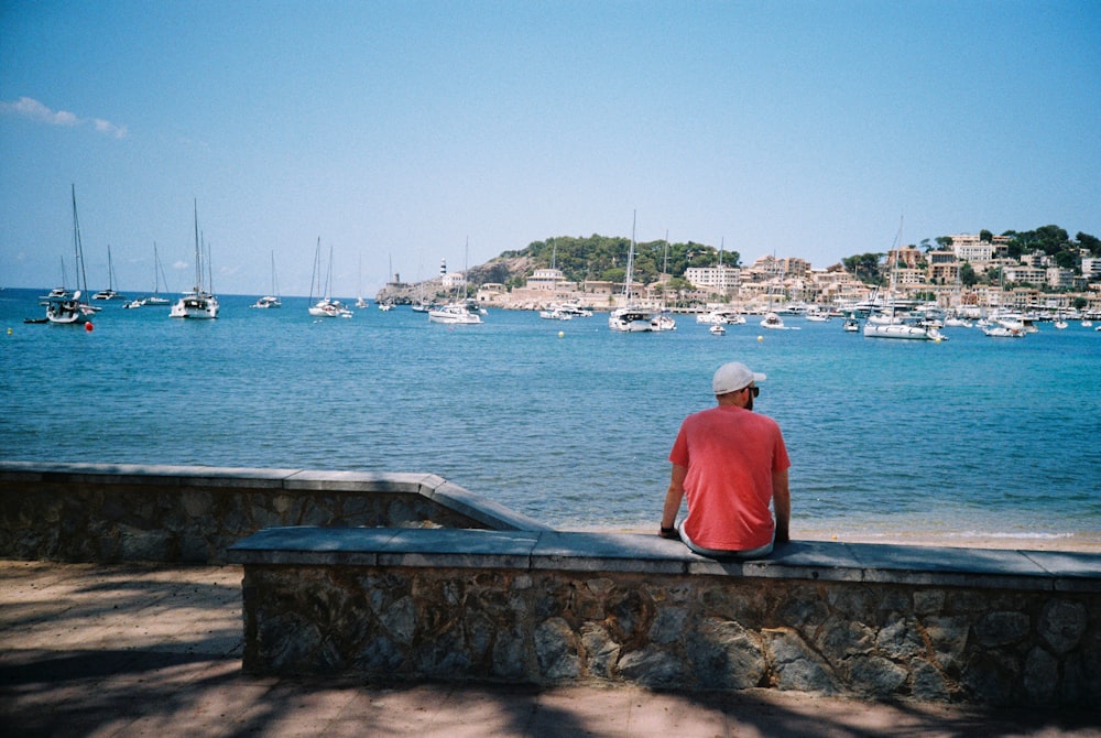 a man sitting on a wall looking out at the water