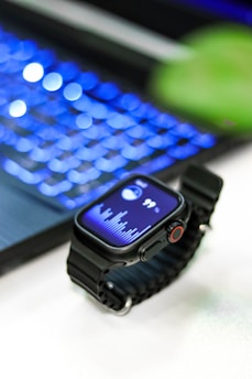 A smartwatch rests near a glowing laptop.