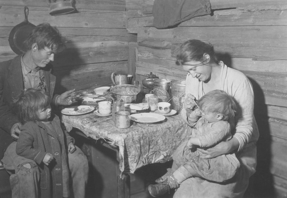 a black and white photo of a woman and two children at a table