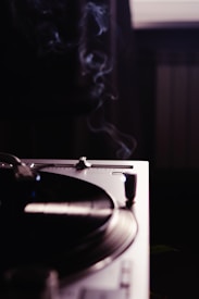 A close-up view of a turntable with a vinyl record spinning, emanating an aura of nostalgia and classic music ambiance. Wisps of smoke rise gently in the dimly lit room, adding a serene and vintage atmosphere.